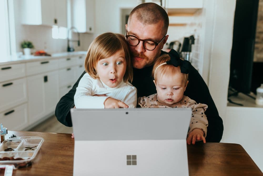 Ein Vater sitzt mit seinen beiden Kindern vor dem Laptop. Er zeigt ihnen, wie einfach die Finanzierung bei Justhome klappt. Die Familie kann bald in ihr eigenes Haus einziehen. Das Kind staunt und ist begeistert.